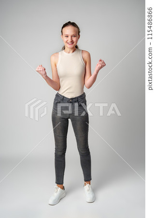 Young Woman in Casual Attire Smiling and Making a Fist Pump Gesture on a Plain Background Young Woman in Casual Attire Smiling and Making a Fist Pump Gesture on a Plain Background 115486866