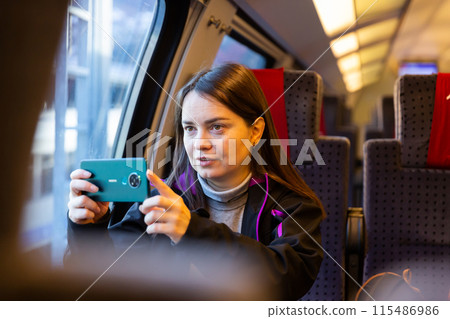 Woman taking photos with smartphone through window glass while travelling by train 115486986
