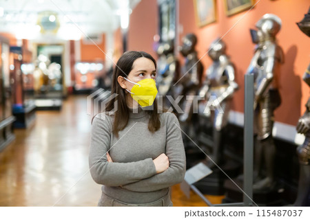 Female museum visitor in protective mask examining ancient armor Female museum visitor in protective mask examining ancient armor 115487037