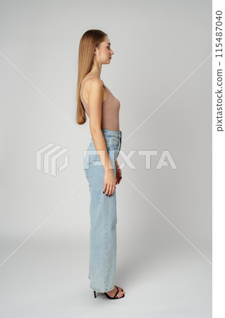Young Woman Wearing High Rise Jeans and Tank Top posing on gray background in studio 115487040