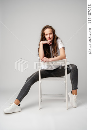 Curly girl model posing on a chair against gray background Curly girl model posing on a chair against gray background 115487058