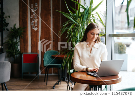 Woman Sitting at Table Using Laptop Computer 115487078