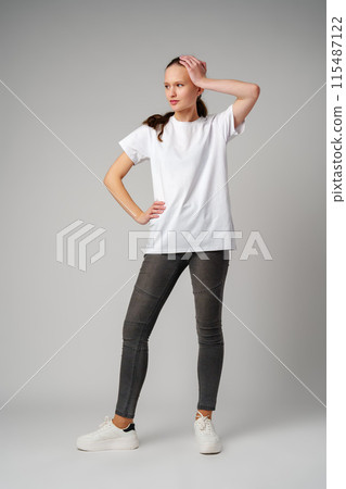 Beautiful young girl posing in white T-shirt and jeans on gray background Beautiful young girl posing in white T-shirt and jeans on gray background 115487122