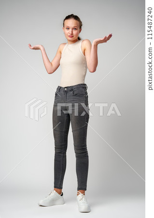 Young Clueless Woman Standing With Outstretched Arms on gray background 115487240