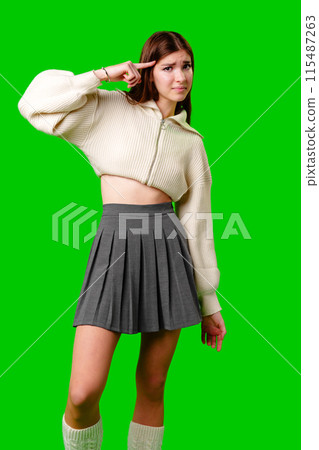 A young woman stands against a vivid green background, exhibiting a confident attitude with one hand behind her head. A young woman stands against a vivid green background, exhibiting a confident attitude with one hand behind her head. 115487263