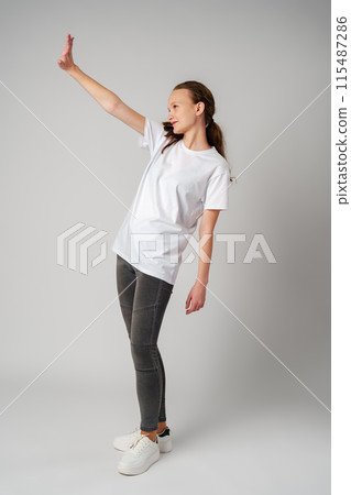 Beautiful young girl posing in white T-shirt and jeans on gray background Beautiful young girl posing in white T-shirt and jeans on gray background 115487286