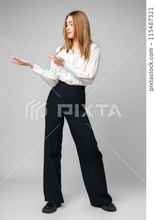 Young blonde woman in formal outfit pointing to the side against gray background 115487321