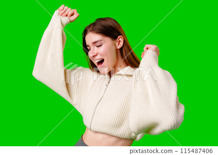 Joyful Young Woman Celebrates With Arms Raised Against Green Screen 115487406