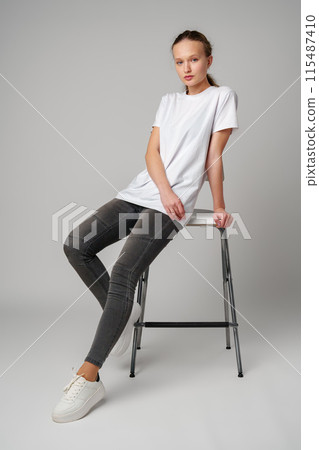 Curly girl model posing on a chair against gray background Curly girl model posing on a chair against gray background 115487410
