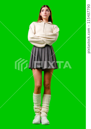 Young Woman in White Sweater and Grey Pleated Skirt Standing Against Green Background 115487790
