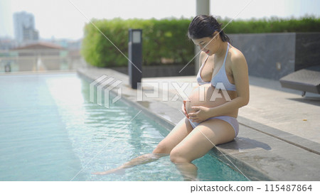 A portrait of happy Asian pregnant woman by the swimming pool. People lifestyle in travel holiday vacation concept. Relaxation. Having a baby. Family people lifestyle. Mom love. A portrait of happy Asian pregnant woman by the swimming pool. People lifestyle in travel holiday vacation concept. Relaxation. Having a baby. Family people lifestyle. Mom love. 115487864