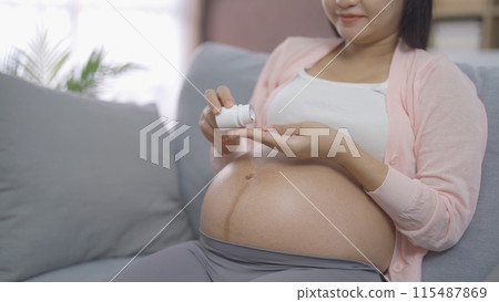 A portrait of happy Asian pregnant woman with medicine pills in bedroom at home. Having a baby. Family people lifestyle. Mom love. A portrait of happy Asian pregnant woman with medicine pills in bedroom at home. Having a baby. Family people lifestyle. Mom love. 115487869