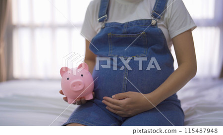 A portrait of happy Asian pregnant woman save financial money for baby with piggy bank in bedroom at home. Having a baby. Family people lifestyle. Mom love. A portrait of happy Asian pregnant woman save financial money for baby with piggy bank in bedroom at home. Having a baby. Family people lifestyle. Mom love. 115487948