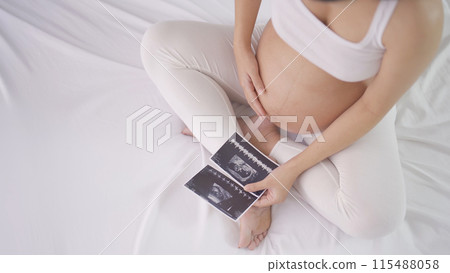A portrait of happy Asian pregnant woman in bedroom at home with baby ultrasound. Having a baby. Family people lifestyle. Mom love. A portrait of happy Asian pregnant woman in bedroom at home with baby ultrasound. Having a baby. Family people lifestyle. Mom love. 115488058