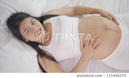 A Portrait of happy Asian pregnant woman in bedroom at home. Having a baby. Family people lifestyle. Love. A Portrait of happy Asian pregnant woman in bedroom at home. Having a baby. Family people lifestyle. Love. 115488274