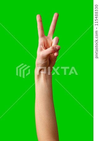 Hand Making Peace Sign Gesture Against Vibrant Green Background 115488330