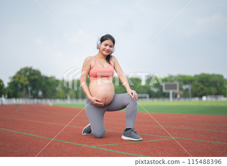 A portrait of happy Asian pregnant woman running on rubber floor, track on a sports stadium. Sport and recreation background. Having a baby. Family people lifestyle. Mom lifestyle. A portrait of happy Asian pregnant woman running on rubber floor, track on a sports stadium. Sport and recreation background. Having a baby. Family people lifestyle. Mom lifestyle. 115488396