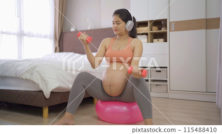 A portrait of happy Asian pregnant woman in bedroom at home. Having a baby. Training workout. Exercise indoor with sport equipment. Athletic. Family people lifestyle. Mom love. Recreation. A portrait of happy Asian pregnant woman in bedroom at home. Having a baby. Training workout. Exercise indoor with sport equipment. Athletic. Family people lifestyle. Mom love. Recreation. 115488410