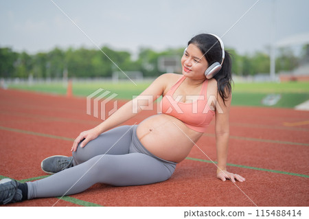 A portrait of happy Asian pregnant woman running on rubber floor, track on a sports stadium. Sport and recreation background. Having a baby. Family people lifestyle. Mom lifestyle. A portrait of happy Asian pregnant woman running on rubber floor, track on a sports stadium. Sport and recreation background. Having a baby. Family people lifestyle. Mom lifestyle. 115488414