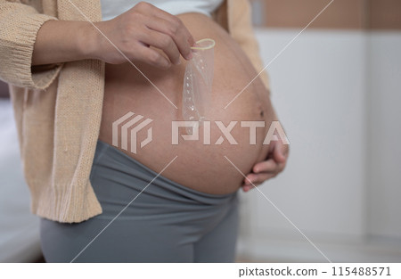 A portrait of happy Asian pregnant woman with condom in bedroom at home. Having a baby. Family people lifestyle. Mom. A portrait of happy Asian pregnant woman with condom in bedroom at home. Having a baby. Family people lifestyle. Mom. 115488571