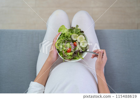 A portrait of happy Asian pregnant woman eating salad vegetable food for dieting in bedroom at home. Having a baby. Family people lifestyle. Mom love. A portrait of happy Asian pregnant woman eating salad vegetable food for dieting in bedroom at home. Having a baby. Family people lifestyle. Mom love. 115488619