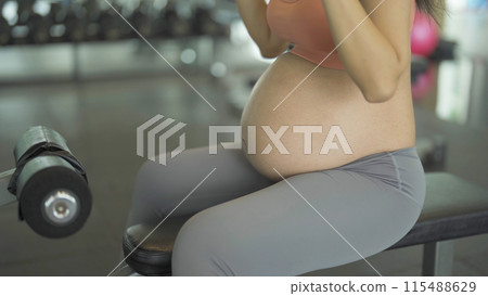 A portrait of happy Asian pregnant woman at gym fitness center club. Having a baby. Training workout. Exercise indoor with sport equipment. Athletic. Family people lifestyle. Mom love. Recreation. A portrait of happy Asian pregnant woman at gym fitness center club. Having a baby. Training workout. Exercise indoor with sport equipment. Athletic. Family people lifestyle. Mom love. Recreation. 115488629