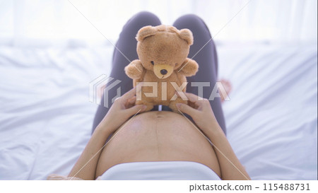A Portrait of happy Asian pregnant woman with a teddy bear in bedroom at home. Having a baby. Family people lifestyle. Love. A Portrait of happy Asian pregnant woman with a teddy bear in bedroom at home. Having a baby. Family people lifestyle. Love. 115488731
