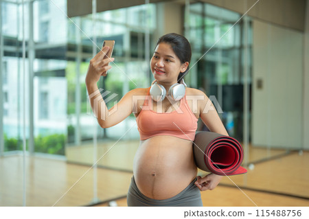 A portrait of happy Asian pregnant woman at gym fitness center club. Having a baby. Training workout. Exercise indoor with sport equipment. Athletic. Family people lifestyle. Mom love. Recreation. A portrait of happy Asian pregnant woman at gym fitness center club. Having a baby. Training workout. Exercise indoor with sport equipment. Athletic. Family people lifestyle. Mom love. Recreation. 115488756