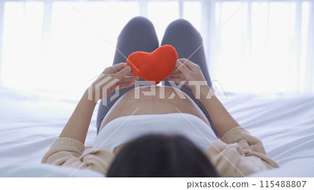 A Portrait of happy Asian pregnant woman with heart in bedroom at home. Having a baby. Family people lifestyle. Love. 115488807