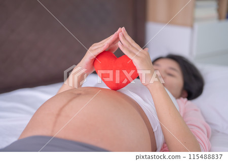 A Portrait of happy Asian pregnant woman with heart in bedroom at home. Having a baby. Family people lifestyle. Love. 115488837