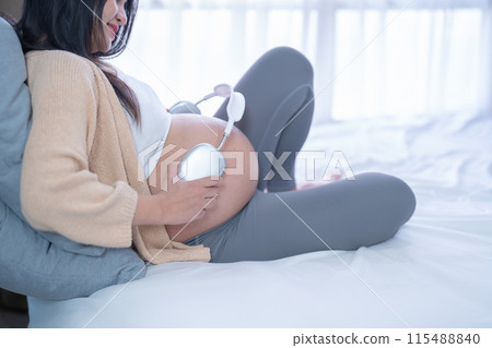 A Portrait of happy Asian pregnant woman listening to music with headphones in bedroom at home. Having a baby. Family people lifestyle. Love. 115488840