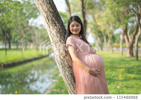 A portrait of happy Asian pregnant woman walking in public garden park on vacation. Love of mother. Having a baby. Family people lifestyle. 115488988