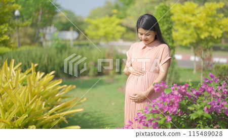 A portrait of happy Asian pregnant woman walking in public garden park on vacation. Love of mother. Having a baby. Family people lifestyle. 115489028