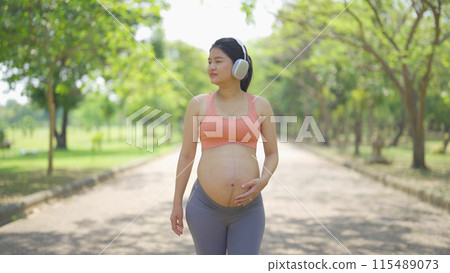 A portrait of happy Asian pregnant woman in yoga class club doing exercise at public garden park. Outdoor sport and recreation. activity with nature trees view. Having a baby. Family people lifestyle. 115489073