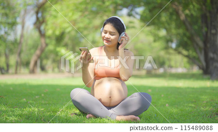 A portrait of happy Asian pregnant woman in yoga class club doing exercise at public garden park. Outdoor sport and recreation. activity with nature trees view. Having a baby. Family people lifestyle. 115489088