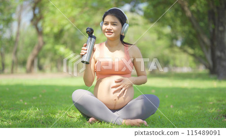 A portrait of happy Asian pregnant woman in yoga class club doing exercise at public garden park. Outdoor sport and recreation. activity with nature trees view. Having a baby. Family people lifestyle. 115489091