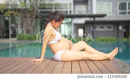 A portrait of happy Asian pregnant woman by the swimming pool. People lifestyle in travel holiday vacation concept. Relaxation. Having a baby. Family people lifestyle. Mom love. A portrait of happy Asian pregnant woman by the swimming pool. People lifestyle in travel holiday vacation concept. Relaxation. Having a baby. Family people lifestyle. Mom love. 115489200