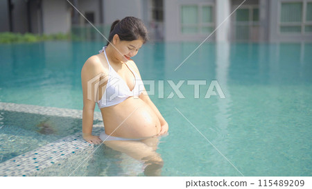 A portrait of happy Asian pregnant woman by the swimming pool. People lifestyle in travel holiday vacation concept. Relaxation. Having a baby. Family people lifestyle. Mom love. A portrait of happy Asian pregnant woman by the swimming pool. People lifestyle in travel holiday vacation concept. Relaxation. Having a baby. Family people lifestyle. Mom love. 115489209