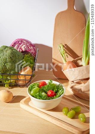 Photo for advertise healthy dish has vegetables, a bowl of vegetable salad displayed on wooden tray next to some fresh tomatoes, decorated with a wooden tray and a black basket of vegetable in back 115489339