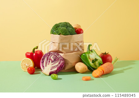 Vegetable theme photo was taken from front angle, against yellow texture. A large paper bag surrounded by fresh vegetables in center on green table top, copy space for text Vegetable theme photo was taken from front angle, against yellow texture. A large paper bag surrounded by fresh vegetables in center on green table top, copy space for text 115489345
