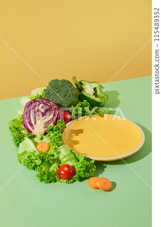 The promotional photo was taken from above view, with a blank yellow dish featured on green countertop, beside decorating with variety vegetables. Empty space for product displaying and adding text 115489352