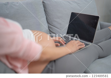 A portrait of happy Asian pregnant woman using, working online with computer laptop notebook tablet device with screen in bedroom at home. Having a baby. Family people lifestyle. Mom love. 115489581