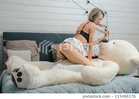 Woman Sitting on Large Stuffed Bear in Bedroom 115490176