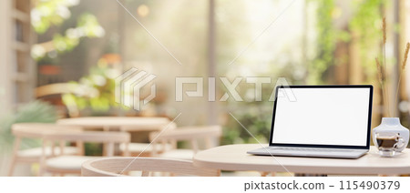 A laptop computer with a white-screen mockup on a table in a beautiful, comfortable coffee shop. 115490379
