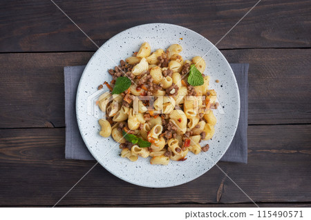 Stewed pasta with minced beef and vegetables, macaroni in Navy style on a plate. Dark wooden background. Copy space. Stewed pasta with minced beef and vegetables, macaroni in Navy style on a plate. Dark wooden background. Copy space. 115490571