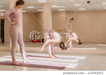 Well looking middle aged sporty woman, fitness instructor in pink sportswear doing stretching and pilates on yoga mat in the studio with mirror. Female fitness yoga. Healthy lifestyle and harmony. 115492051