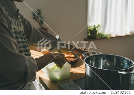 A housewife cooking with torn lettuce stored in a food storage container 115492102