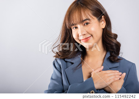 A happy business woman in casual attire holds her hands close to her chest, meditating and smiling. Studio shot isolated on a white background, portraying the concepts of belief, faith, and gratitude 115492242