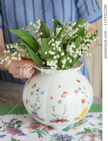 Female put bouquet of lilies of valley in vase 115492299