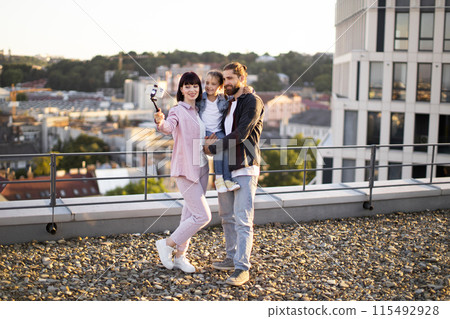 Happy family taking selfie on urban rooftop during sunset 115492928